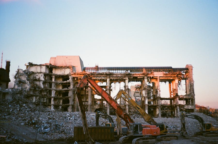 A partially demolished building at sunset, with heavy machinery and debris scattered around the site, showcasing urban decay.